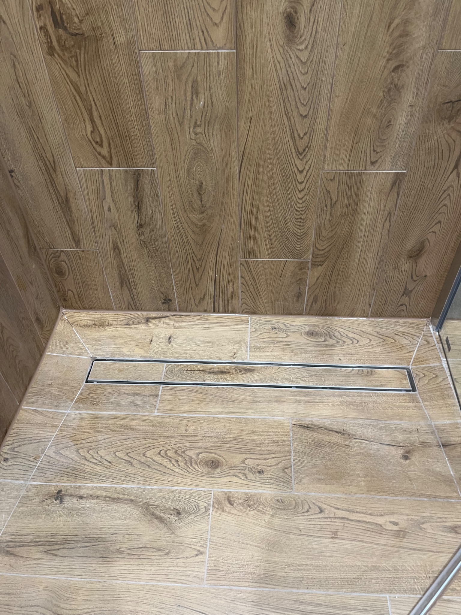 Wykończona kabina prysznicowa z odpływem liniowym i okładziną z płytek imitujących drewno na ścianach i podłodze.