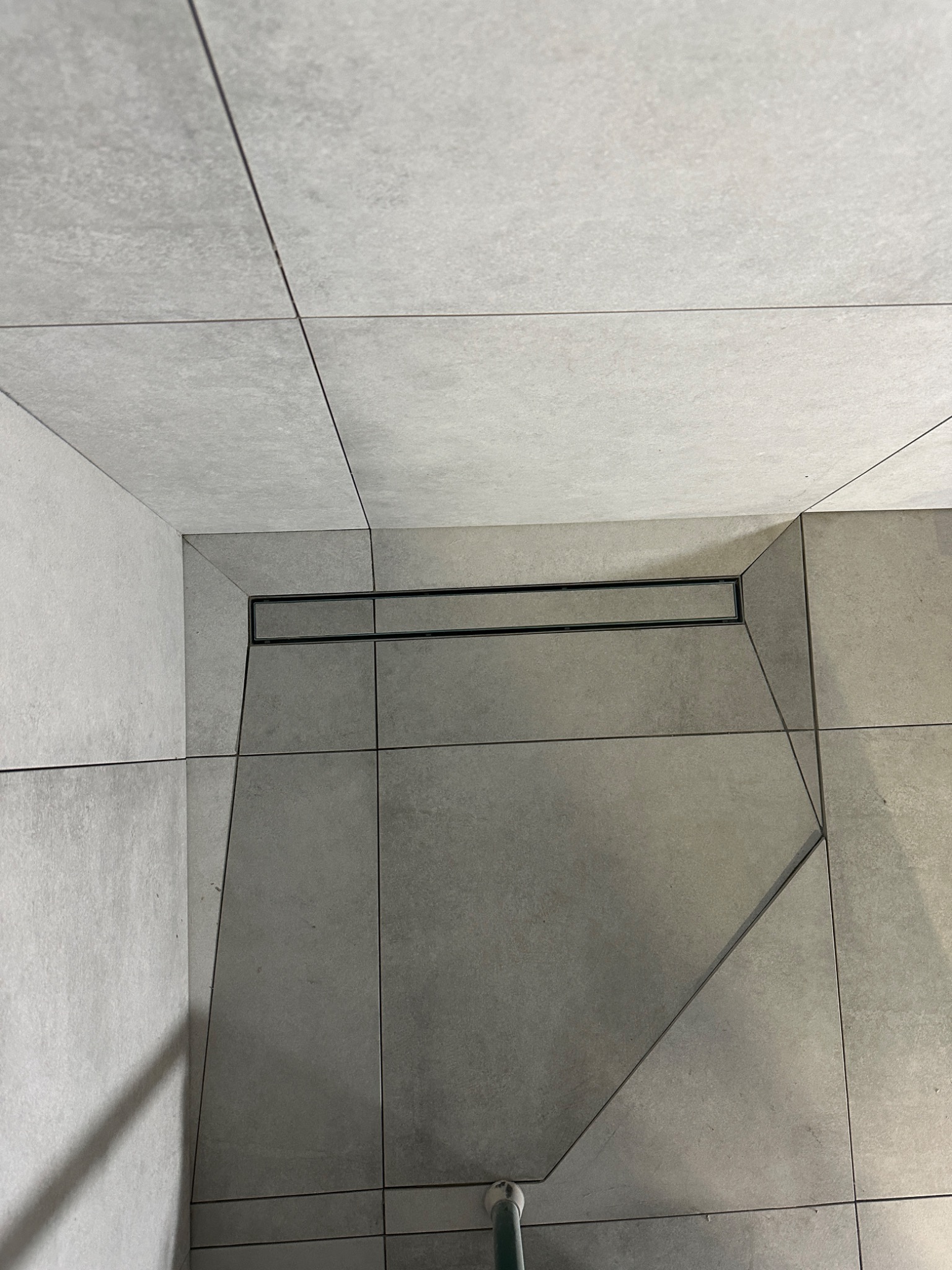 Szare płytki podłogowe w łazience z odpływem liniowym w czarnej ramce, ułożone z precyzyjnym spadkiem w kierunku odpływu.