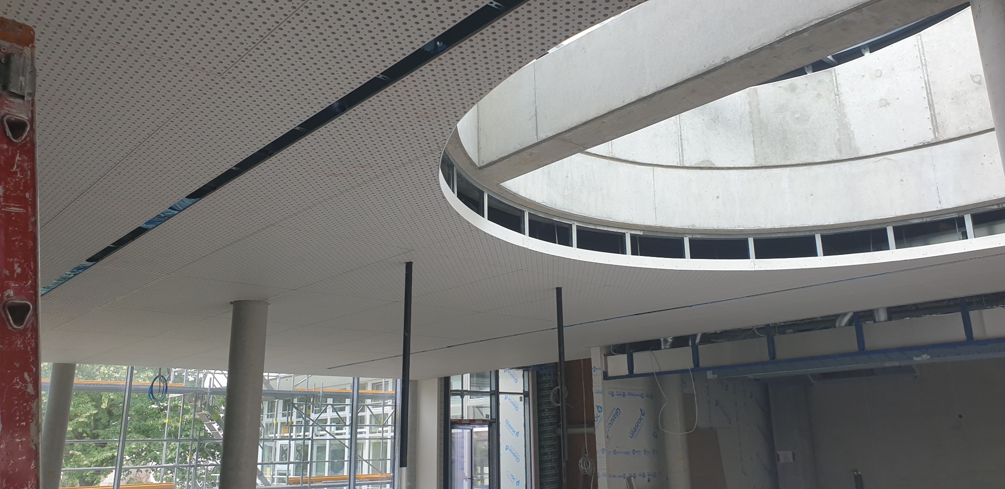 Montaż sufitu podwieszanego z okrągłym świetlikiem w budynku komercyjnym, widoczne elementy konstrukcyjne i drabina po lewej stronie.