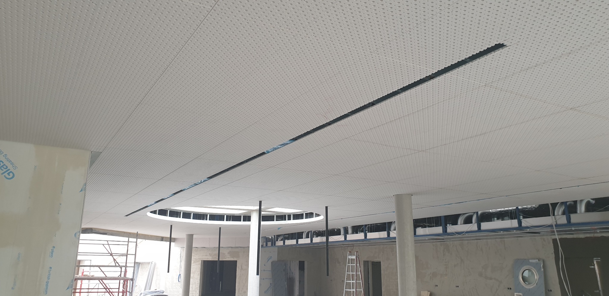 Montaż sufitu podwieszanego z perforowanymi płytami, widoczne profile i instalacje nad sufitem, elementy konstrukcyjne budynku w tle.