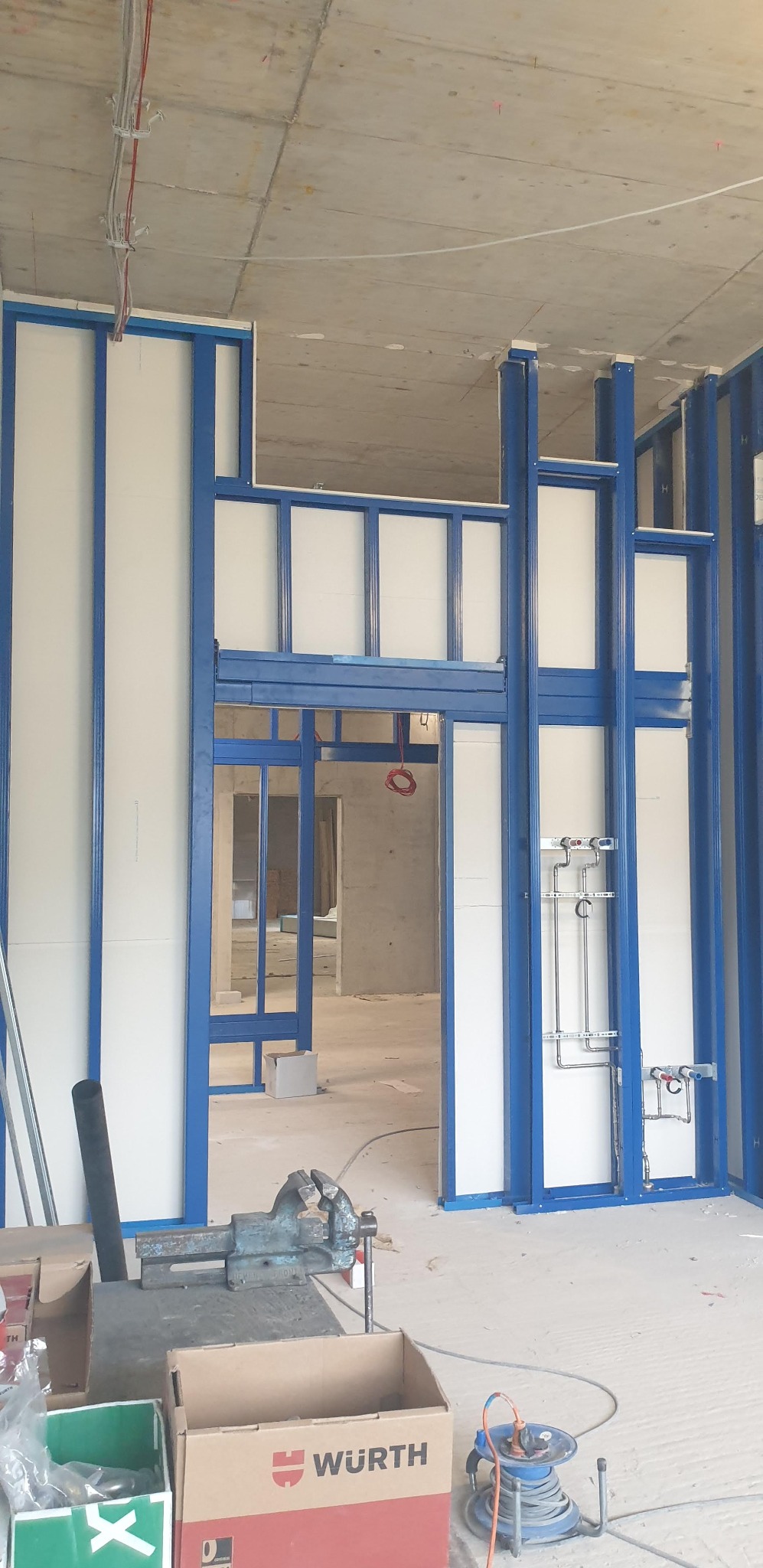 Montaż ścian działowych z płyty karton-gips na metalowym stelażu z widoczną instalacją hydrauliczną w surowym stanie deweloperskim.