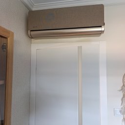 KD Install - Beżowy klimatyzator Rotenso zamontowany nad białymi drzwiami w pomieszczeniu o jasnej ścianie z wzorem. Widoczny fragment drzwi i dekoracja na ścianie.