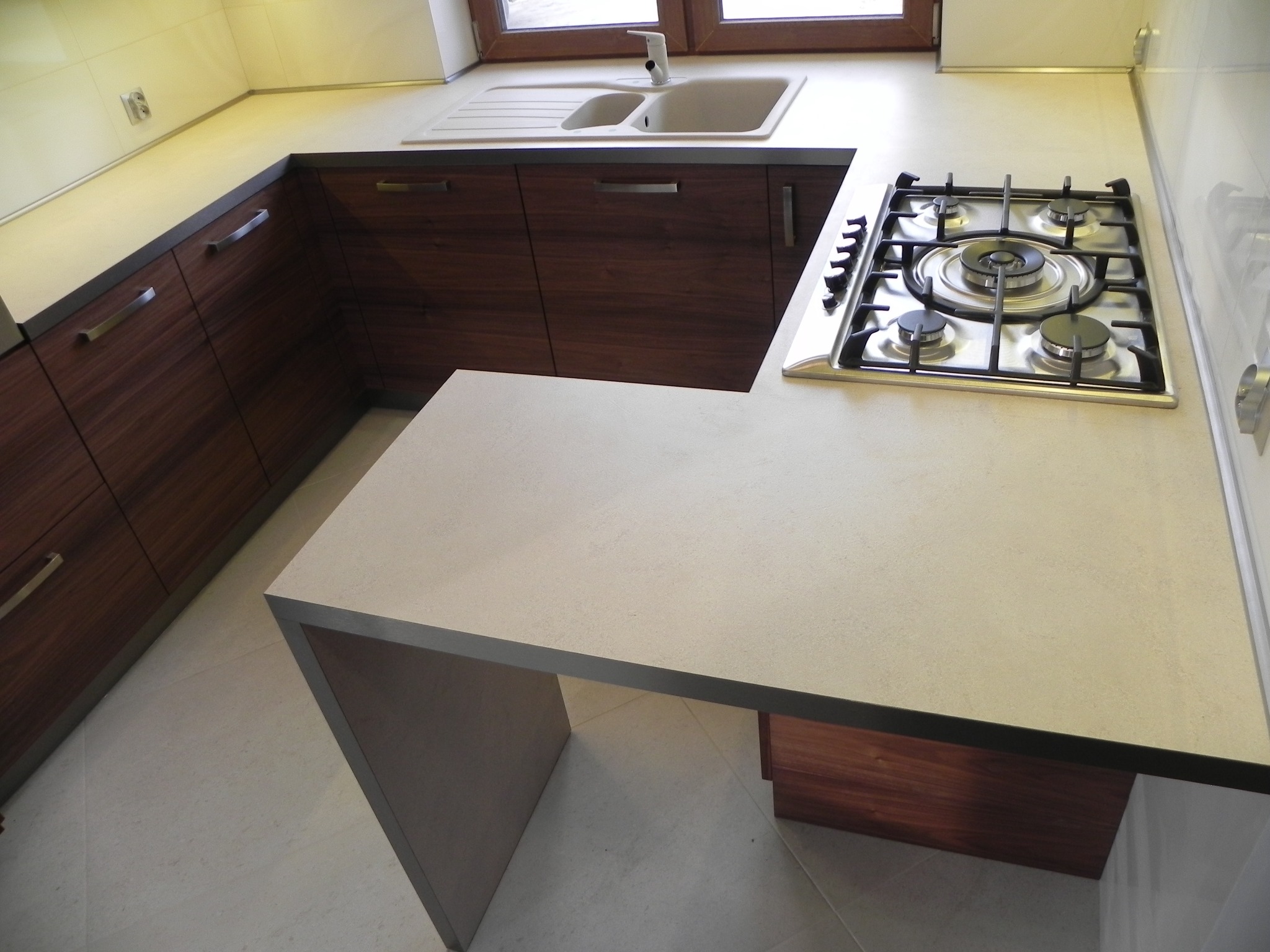 Nowoczesna kuchnia z drewnianymi szafkami, jasnym blatem, zlewem i płytą gazową.