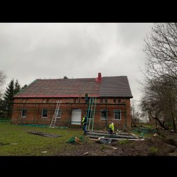 Zakład Ogólnobudowlany Dariusz Misiura - Ekipa budowlana w Darłowie podczas prac na dachu ceglanego domu, widoczne rusztowania, drabiny i częściowo położone nowe pokrycie.