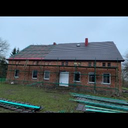 Zakład Ogólnobudowlany Dariusz Misiura - Częściowo wymieniony dach z ciemnej dachówki na ceglanym budynku gospodarczym, rusztowania wokół, przygotowane elementy dachowe na trawie.