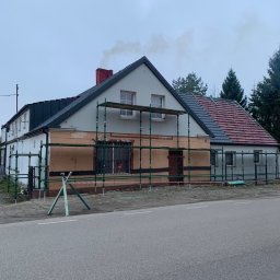 Zakład Ogólnobudowlany Dariusz Misiura - Dom jednorodzinny w trakcie prac dekarskich, widoczne rusztowania, część dachu pokryta nową dachówką, z komina unosi się dym.