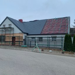 Zakład Ogólnobudowlany Dariusz Misiura - Dom w trakcie remontu dachu: część dachu pokryta szarą dachówką, druga część z widoczną konstrukcją i folią. Rusztowania wokół budynku, pochmurne niebo.