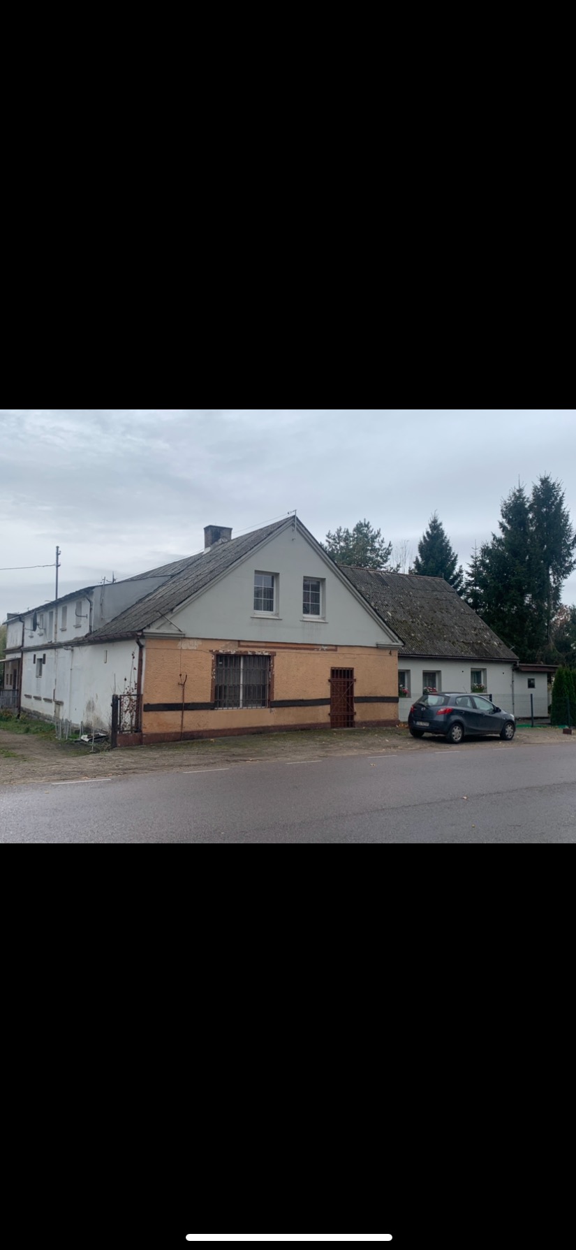 Dwukondygnacyjny budynek z szarym dachem i pomarańczową elewacją poniżej, widok z zewnątrz, pochmurny dzień.