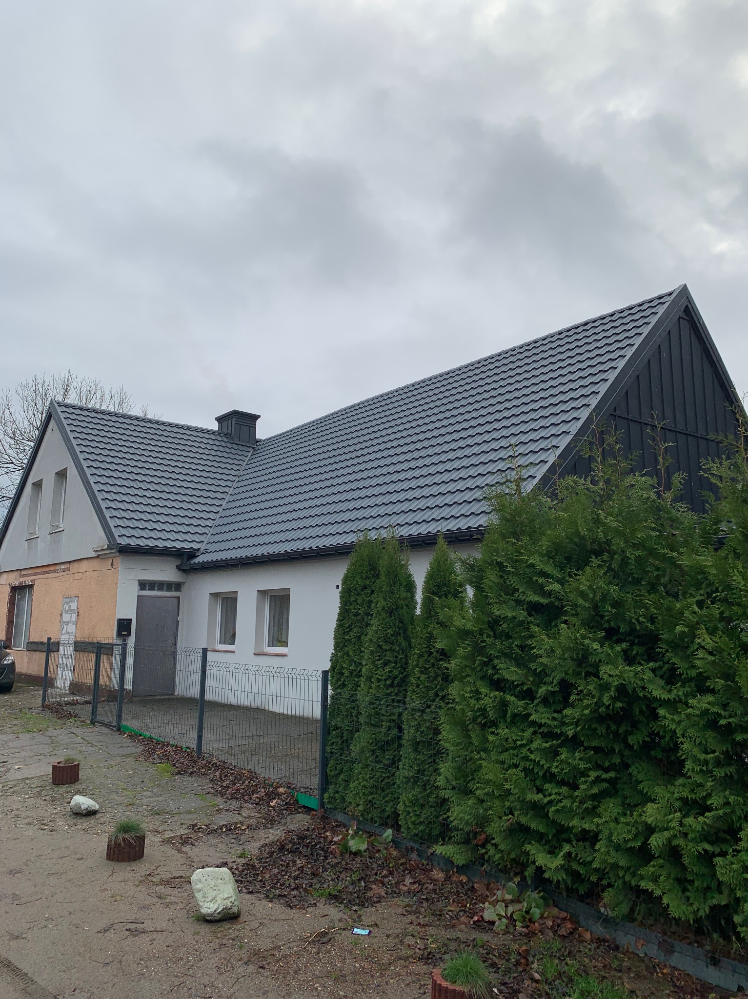 Dom jednorodzinny z nowym, ciemnoszarym dachem z blachodachówki modułowej, widok z zewnątrz, pochmurne niebo w tle.