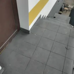 Szare płytki na schodach zewnętrznych prowadzących do drzwi, z widocznym fragmentem elewacji z żółtym pasem.