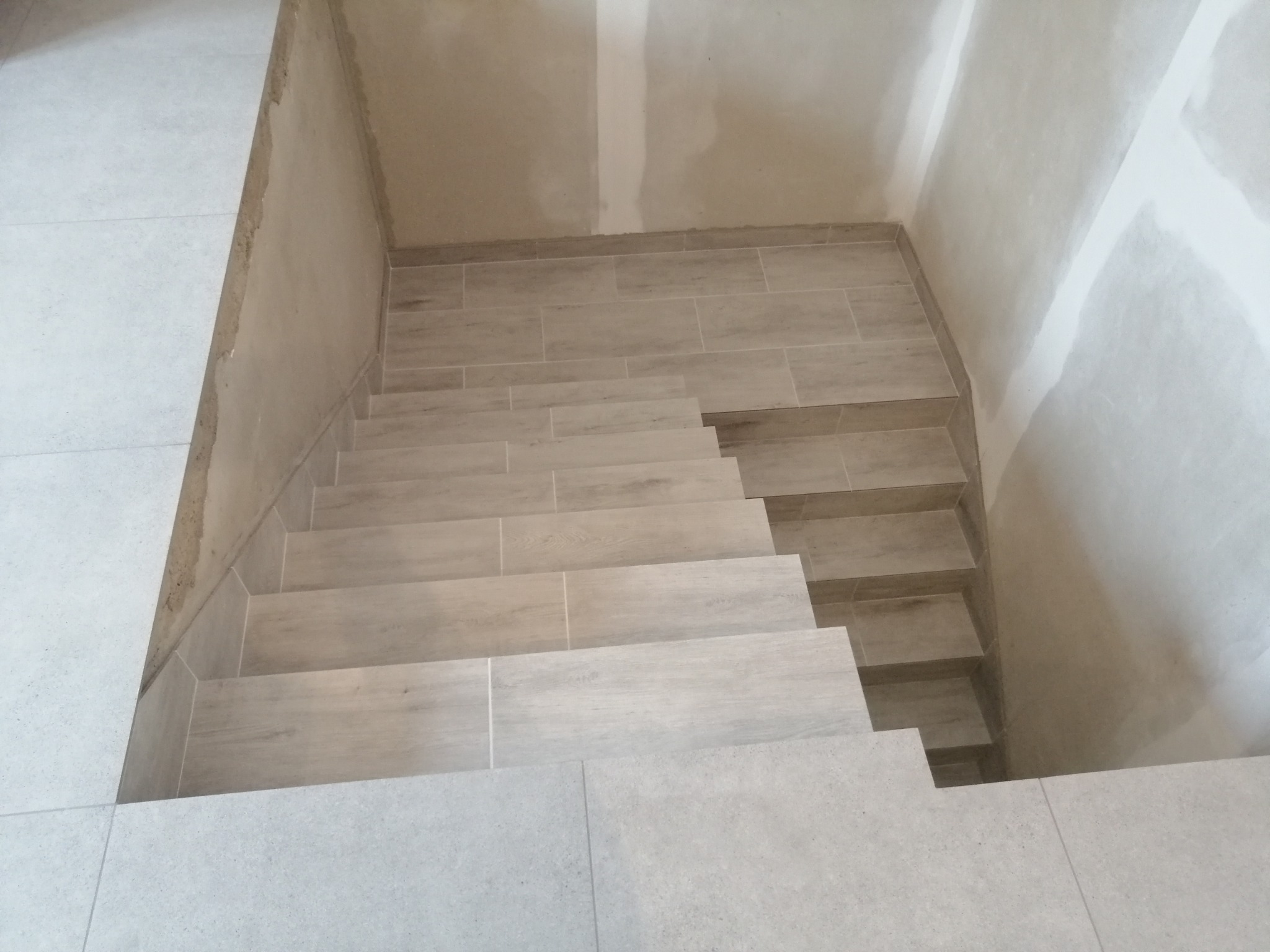 Wykończone schody wewnętrzne wyłożone płytkami imitującymi drewno, widoczne łączenia płyt na stopniach, ściany w surowym stanie, przygotowane do malowania.