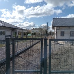 DB.Building Dominik Budzyński Usługi Wypożyczalnia - Nowoczesne ogrodzenie panelowe w kolorze grafitowym, z widoczną furtką i betonową podmurówką, otaczające posesję z domami w trakcie budowy, na tle błękitnego nieba.