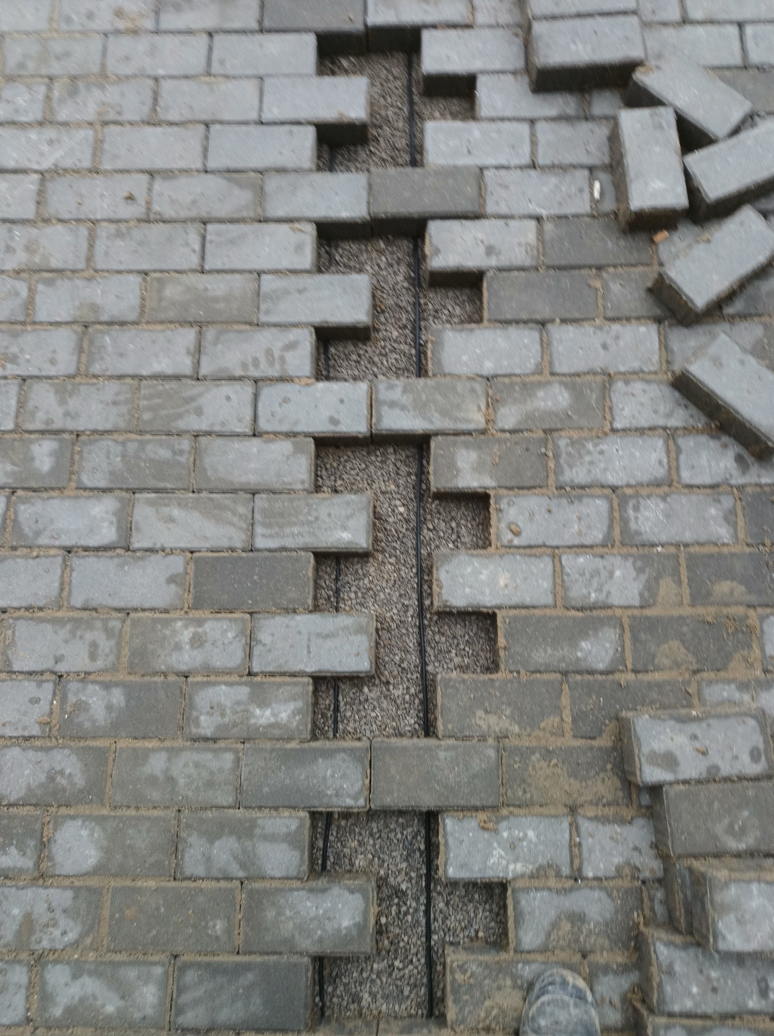 Układanie szarej kostki brukowej na podsypce w Żdżarce, widoczne przerwy w ułożeniu i kabel w szczelinie. Częściowo ułożona nawierzchnia z kostki.