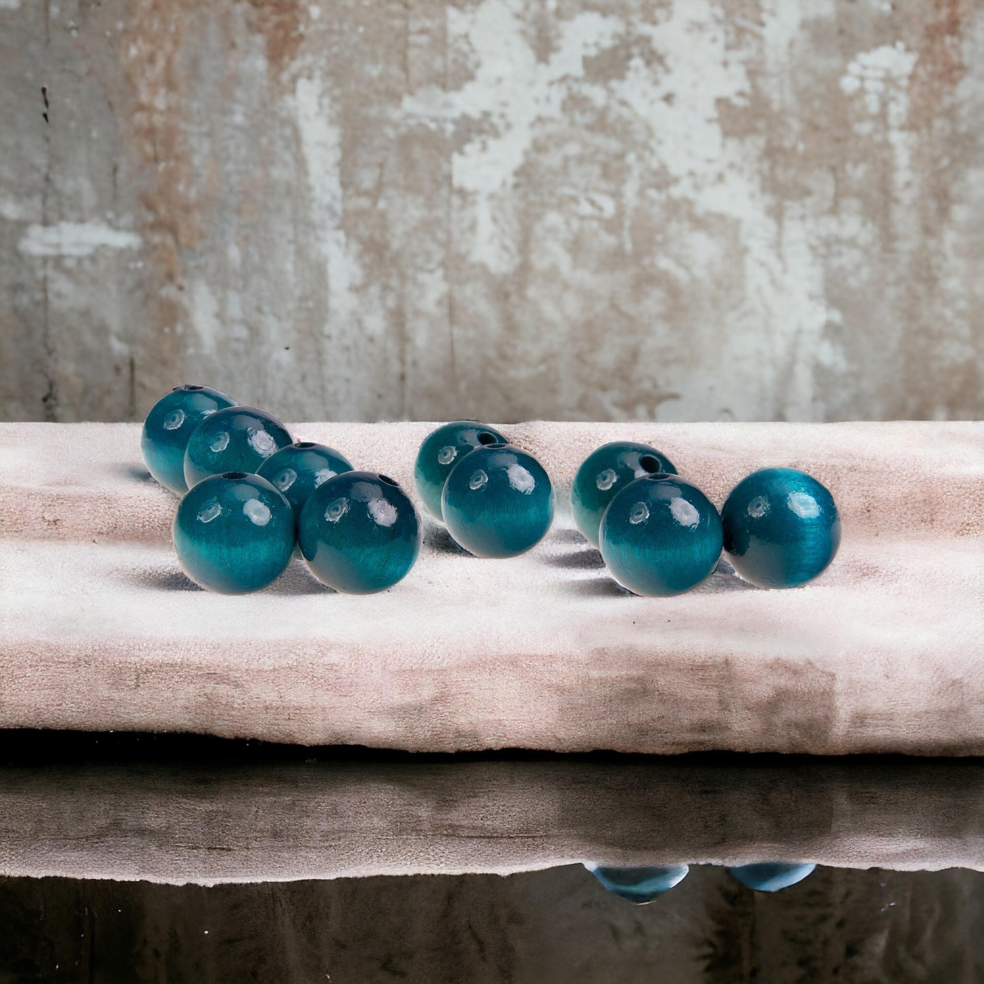 Błyszczące, turkusowe, drewniane koraliki z widocznymi otworami, ułożone na kremowym materiale, z refleksami na ciemnym tle.