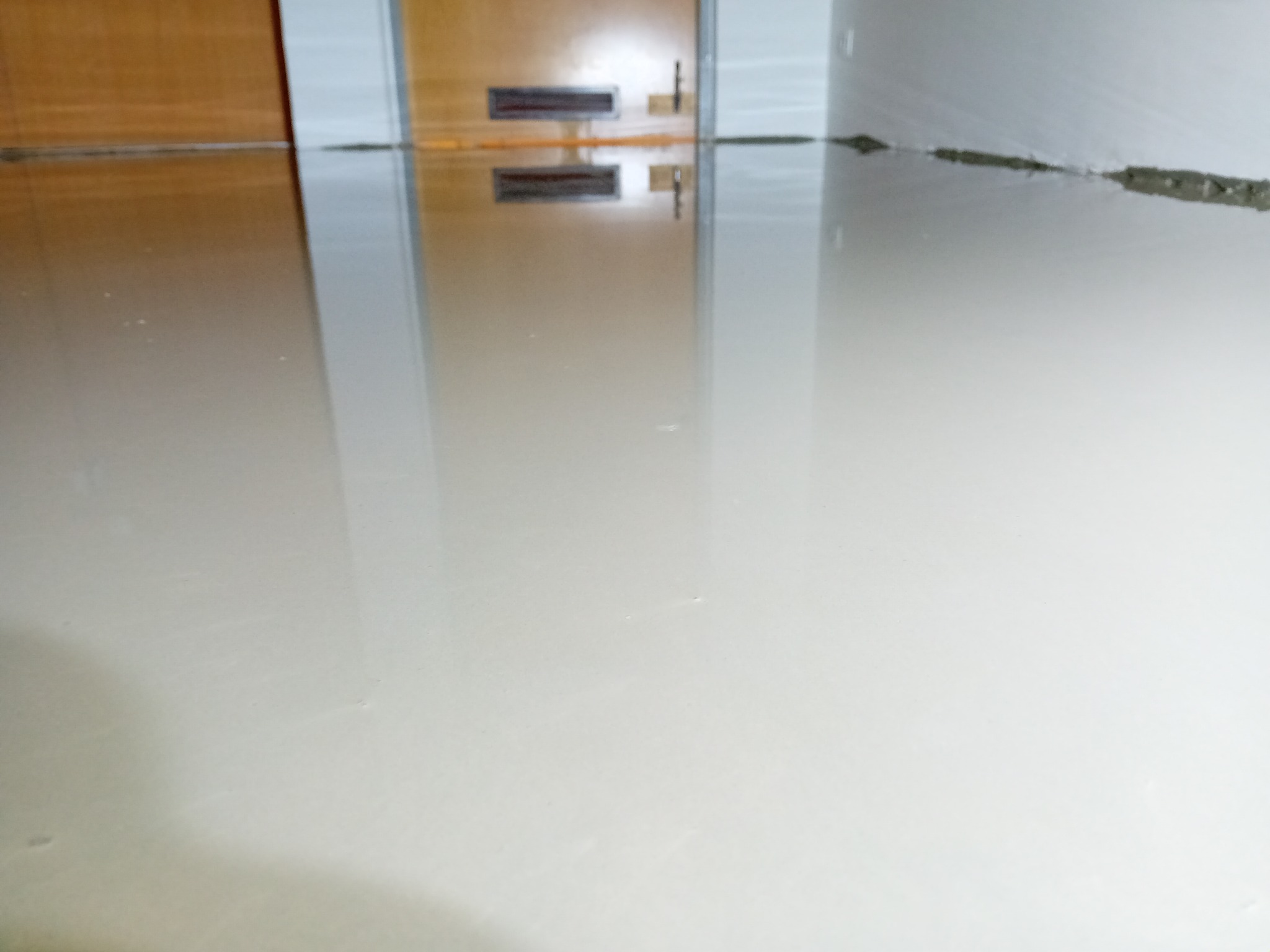 Wylewka samopoziomująca na podłodze, odbijająca drzwi i fragment ściany, przygotowana pod dalsze prace wykończeniowe.