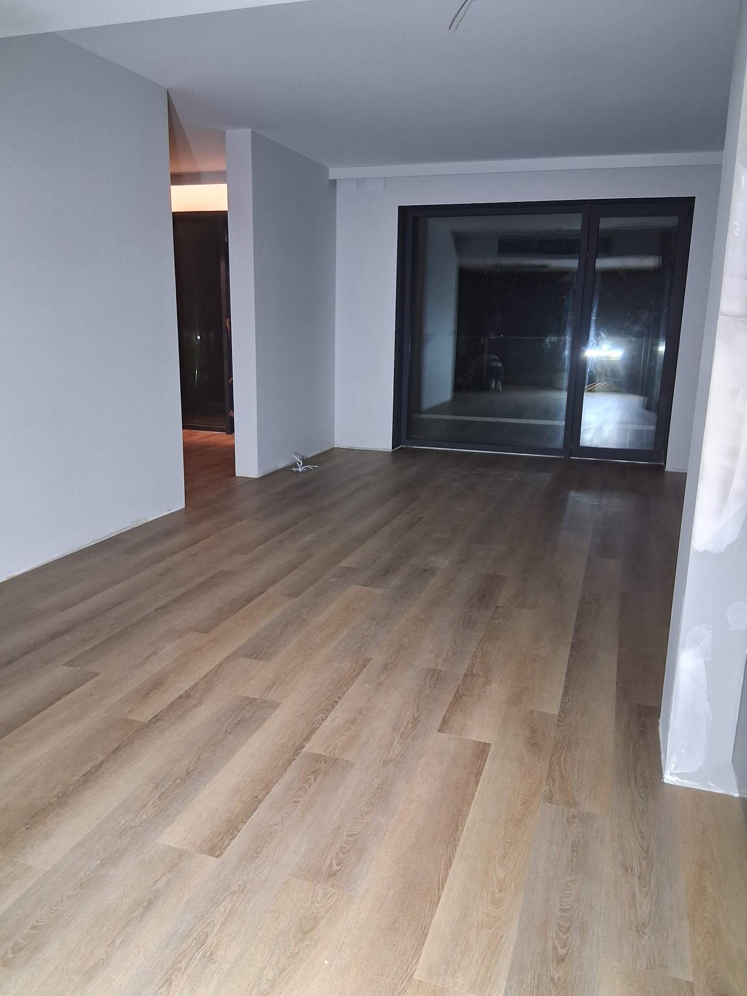 Jasne panele podłogowe ułożone w nowym pokoju z dużym oknem balkonowym, widoczne świeże malowanie ścian.