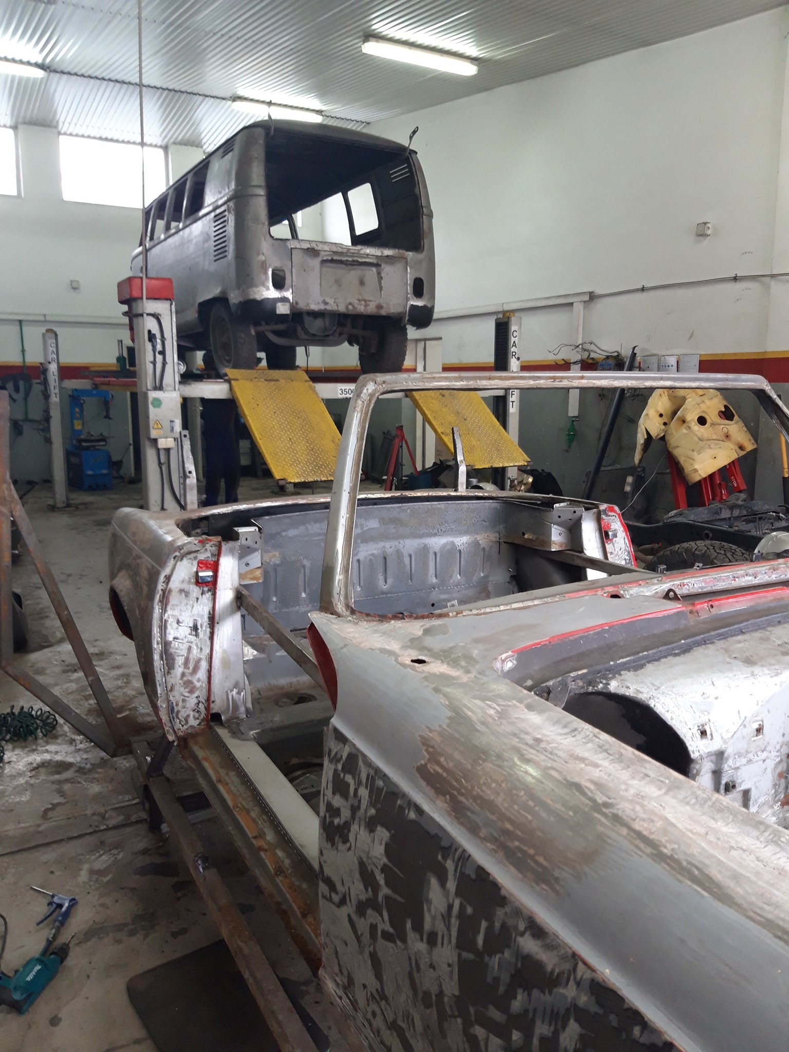 Warsztat samochodowy: karoseria odrestaurowywanego kabrioletu w trakcie prac blacharskich, w tle podnośnik z VW Transporterem.