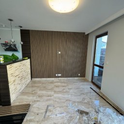 ELMAL - Wnętrze w trakcie wykańczania: panel ścienny z pionowych listew, marmurowe płytki podłogowe, widoczne narzędzia i folie ochronne. Nowoczesne oświetlenie sufitowe.