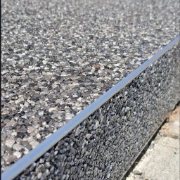 ELMAL - Szara, kamienna posadzka z metalową listwą wykończeniową, wykonana z żywicy epoksydowej i kruszywa. Widoczne drobne kamyczki i struktura powierzchni.