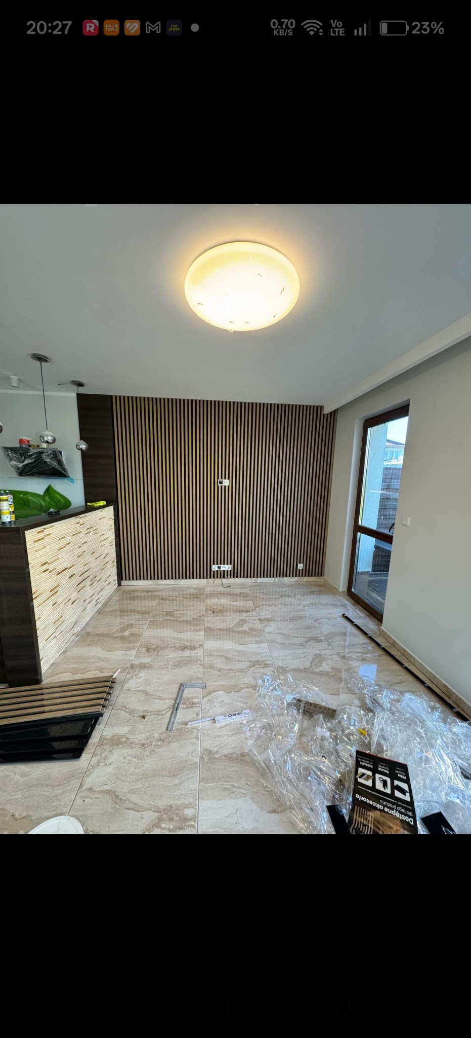 Wnętrze w trakcie wykańczania: panel ścienny z pionowych listew, marmurowe płytki podłogowe, widoczne narzędzia i folie ochronne. Nowoczesne oświetlenie sufitowe.