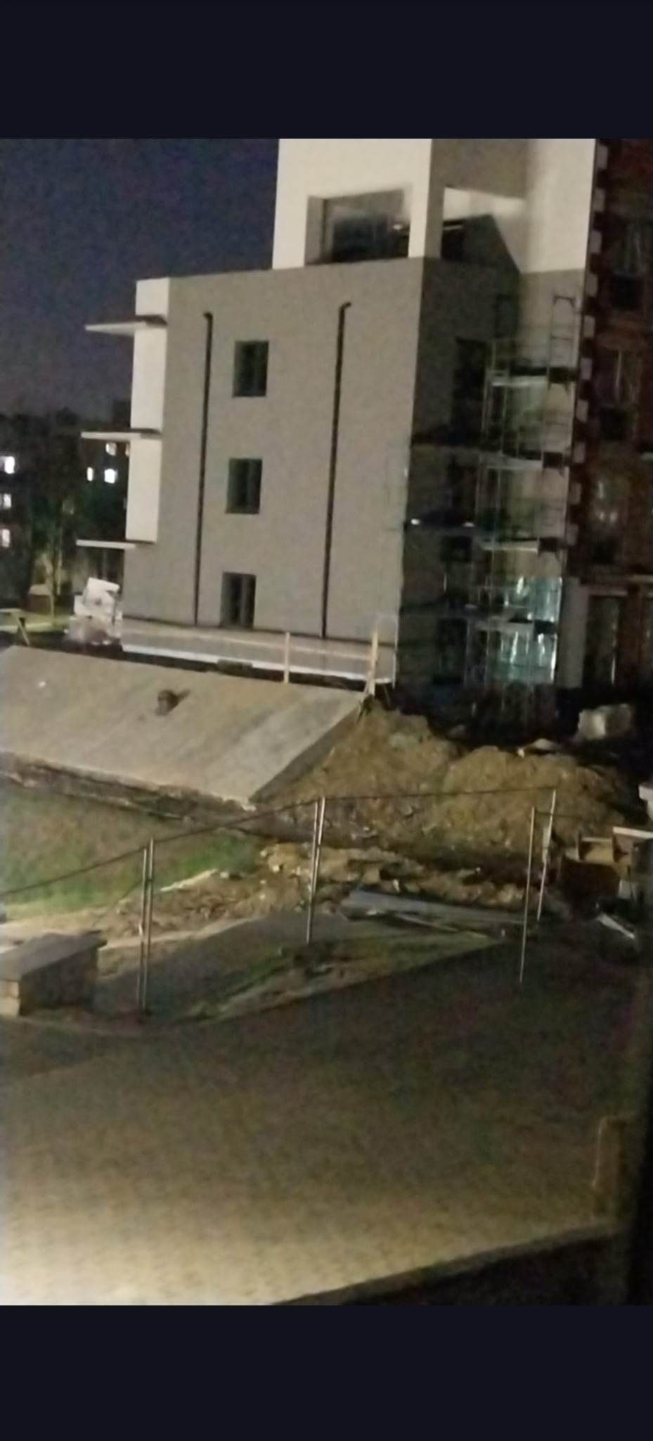 Nocne ujęcie budynku w trakcie prac elewacyjnych, widoczne rusztowania i teren budowy. Oświetlenie uliczne i okna w tle.