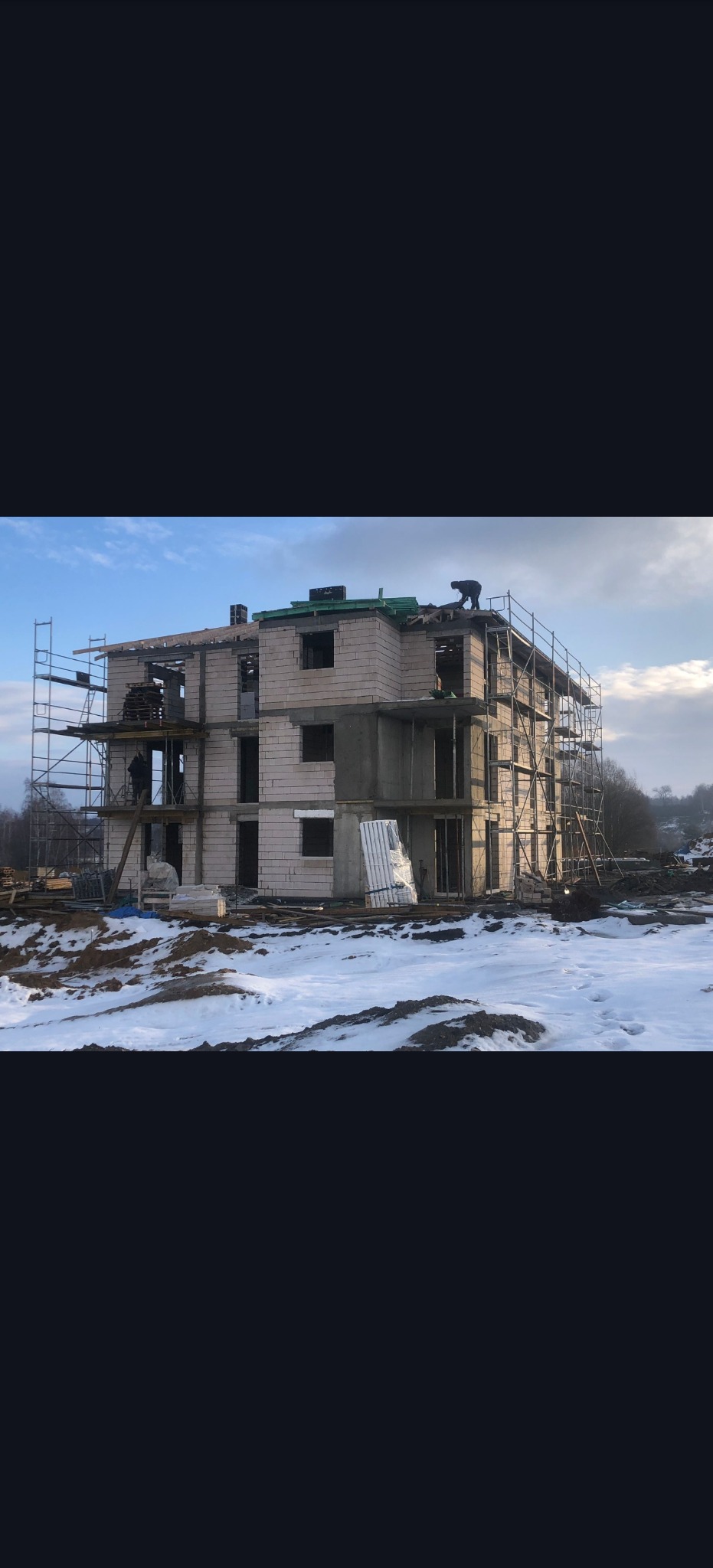 Budowa bloku mieszkalnego w Tychach, w trakcie prac murarskich. Widoczne rusztowania i pracownicy na dachu. Zimowy krajobraz z resztkami śniegu.