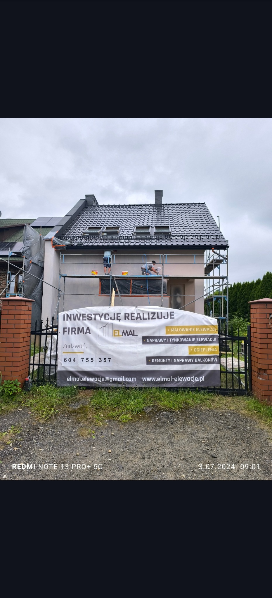 Dom w trakcie malowania elewacji, widoczni pracownicy na rusztowaniu. Na pierwszym planie baner reklamowy firmy z ofertą malowania, napraw i remontów balkonów.