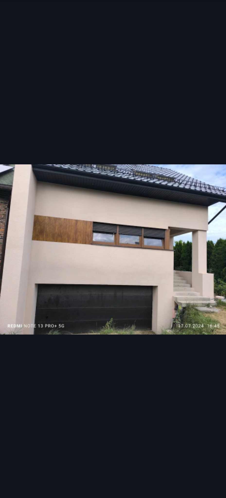 Elewacja domu jednorodzinnego po malowaniu w beżowym kolorze, z drewnianym akcentem i czarną bramą garażową. Widoczne schody wejściowe i fragment dachu.