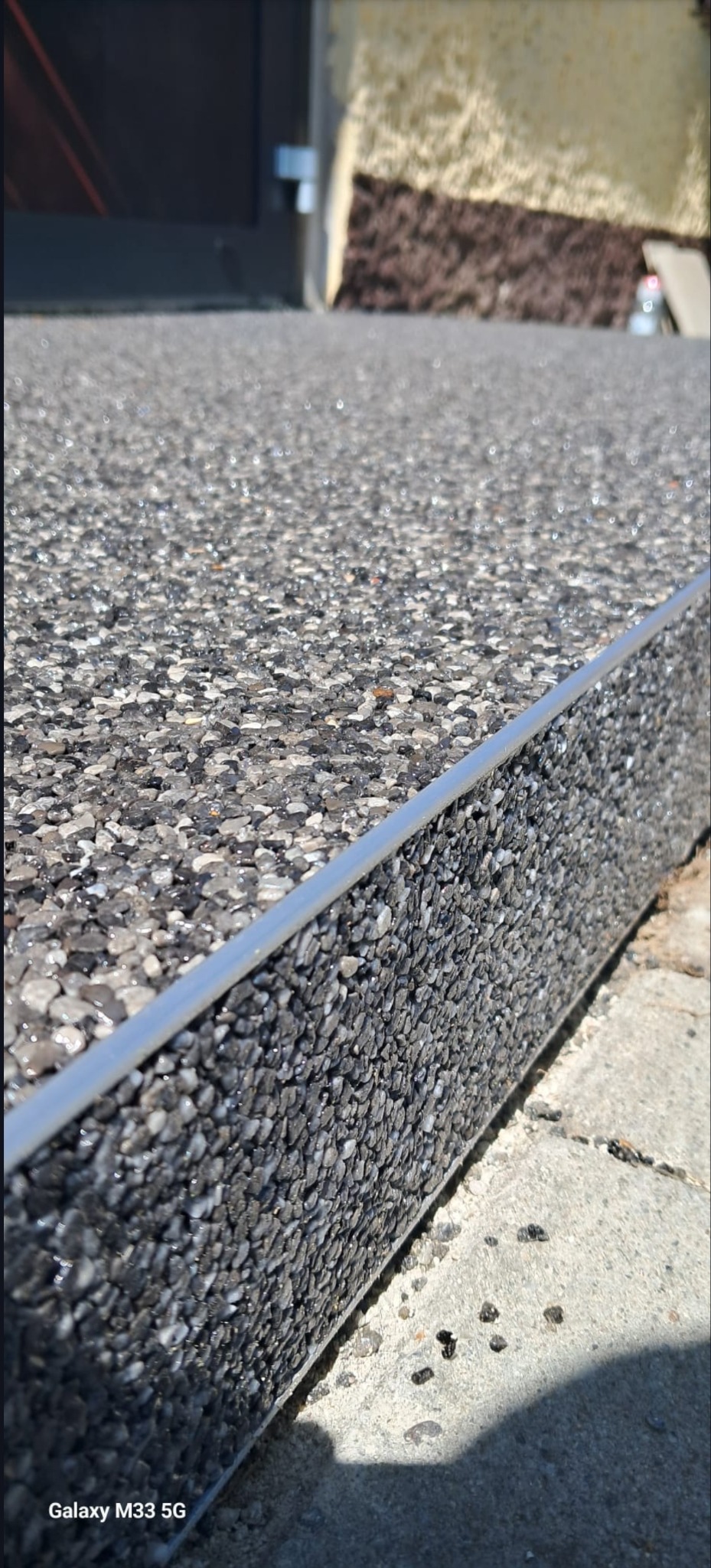 Szara, kamienna posadzka z metalową listwą wykończeniową, wykonana z żywicy epoksydowej i kruszywa. Widoczne drobne kamyczki i struktura powierzchni.