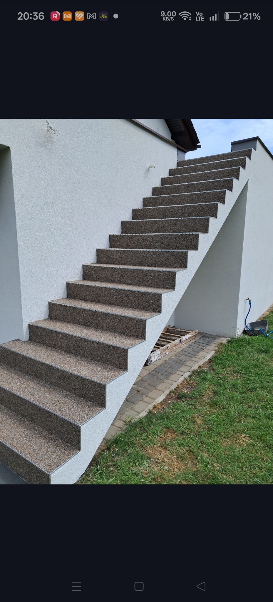 Zewnętrzne schody z wykończeniem z żywicy kamiennej, prowadzące do budynku z jasną elewacją. Widoczne detale wykończeniowe i otoczenie z zielonym trawnikiem.