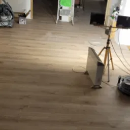 Wnętrze w trakcie prac wykończeniowych: ułożone panele podłogowe, przygotowane ściany, drabina malarska, oświetlenie robocze i sprzęt budowlany.