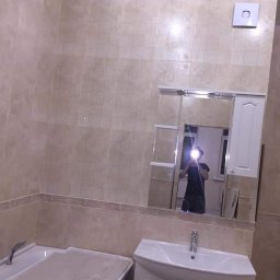 SLAVLEN GRUP Viacheslav Kudinov - Wykończona łazienka z beżowymi płytkami, białą umywalką z szafką i wanną, widoczne odbicie osoby robiącej zdjęcie w lustrze.