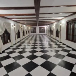 Przestronne wnętrze z podłogą w czarno-białą szachownicę, drewnianymi belkami stropowymi i oknami z kremowymi zasłonami.