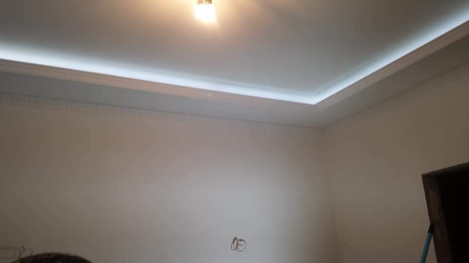 Wykończony sufit podwieszany z oświetleniem LED i dekoracyjnym gzymsem, białe ściany w pomieszczeniu przed umeblowaniem.