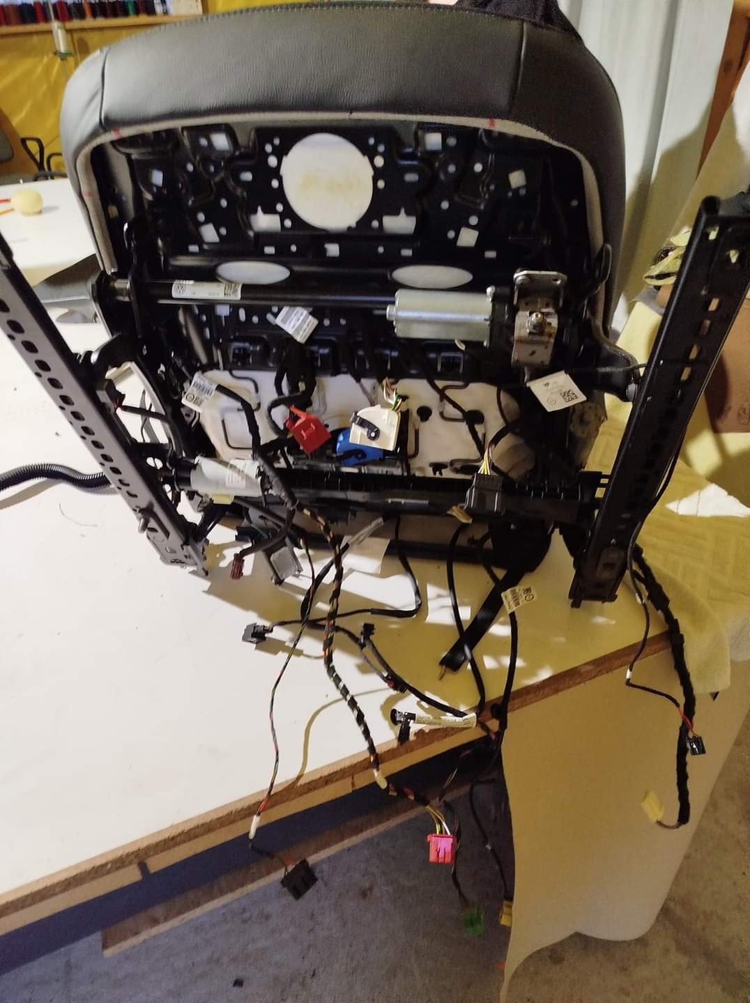 Rozmontowany fotel samochodowy z widocznymi mechanizmami i przewodami elektrycznymi podczas prac tapicerskich.
