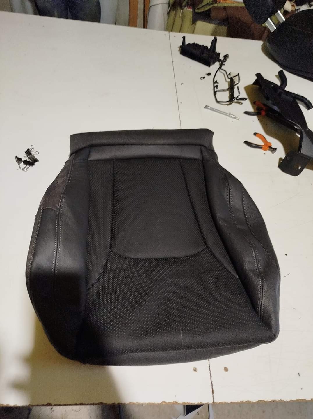 Czarne skórzane siedzisko samochodowe z elementami elektronicznymi i narzędziami na białym stole warsztatowym.