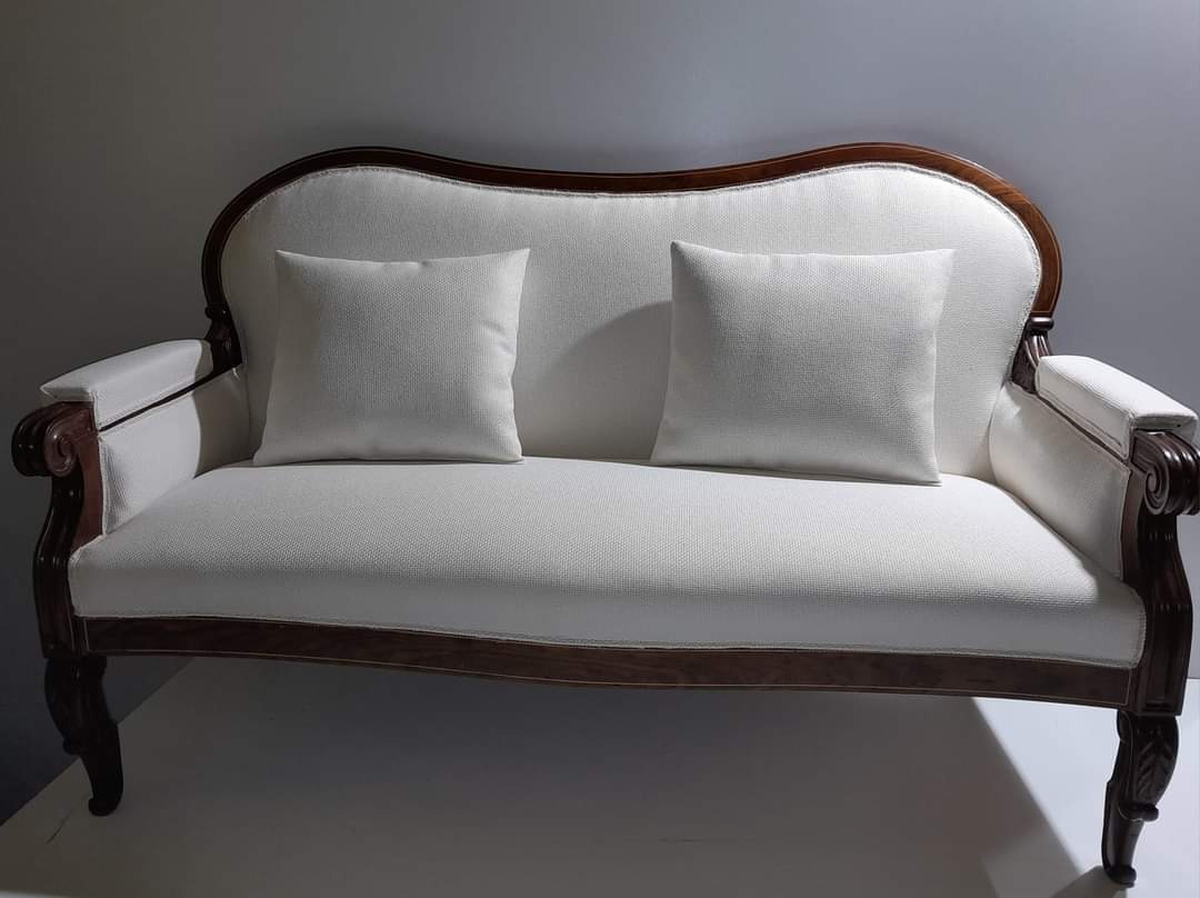 Dwuosobowa sofa w stylu retro z ciemnobrązowym drewnianym wykończeniem i jasną tapicerką z dwoma kwadratowymi poduszkami.