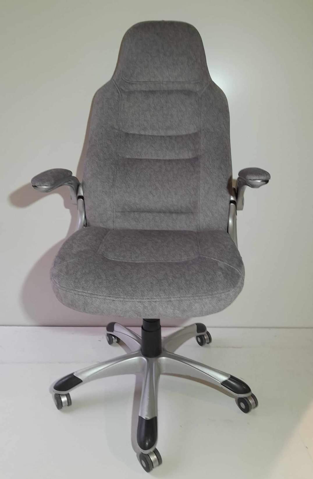 Szare, tapicerowane krzesło biurowe z regulowanymi podłokietnikami i srebrną podstawą na kółkach, sfotografowane na białym tle.