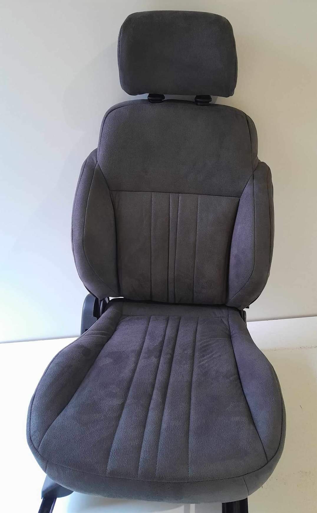 Szare, welurowe siedzenie samochodowe z zagłówkiem, widok z przodu, z pionowymi przeszyciami na siedzisku i oparciu.