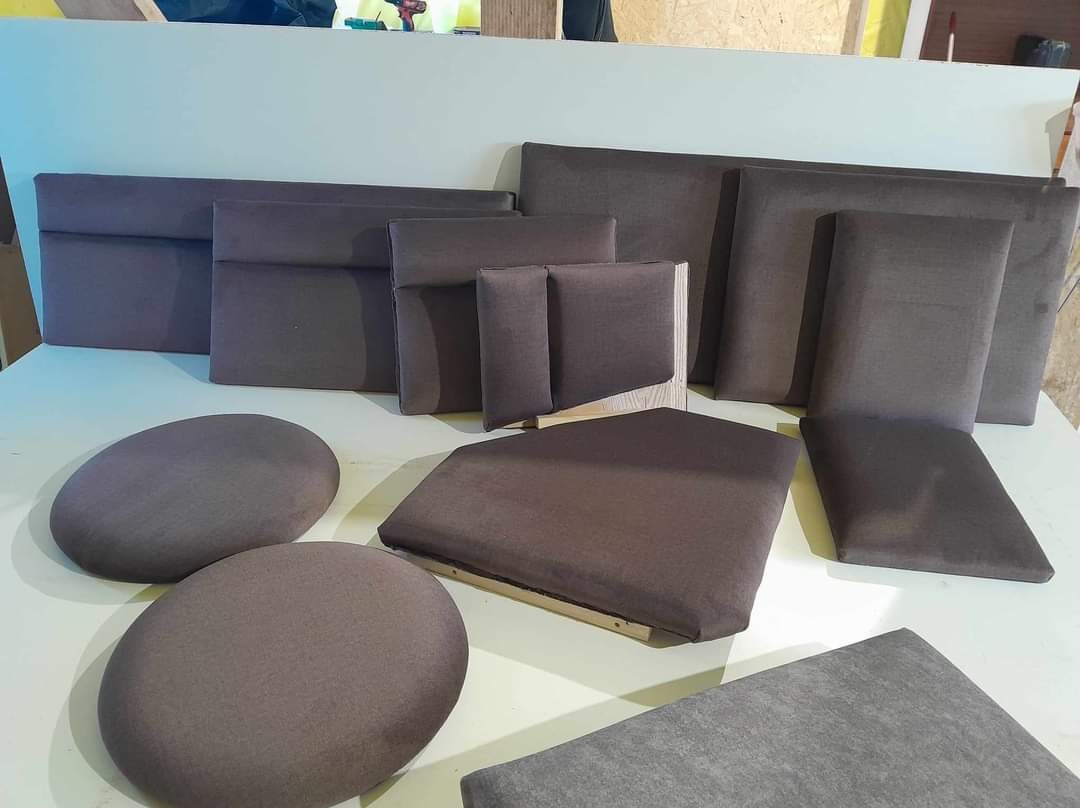 Elementy mebli tapicerowanych w odcieniach szarości, w tym zagłówki, siedziska i oparcia krzeseł, widoczne drewniane ramy niektórych elementów.