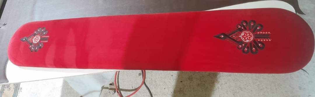 Czerwona, tapicerowana ławka z ozdobnymi, symetrycznymi wzorami po bokach, umieszczona na białym podłożu.