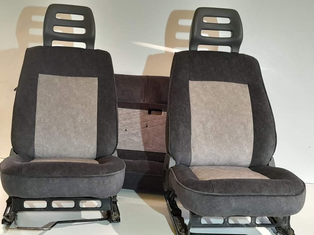 Dwa odnowione fotele samochodowe z szarą tapicerką i zagłówkami oraz panel tapicerowany z wzorem w tle, ukazujące efekt renowacji tapicerki.