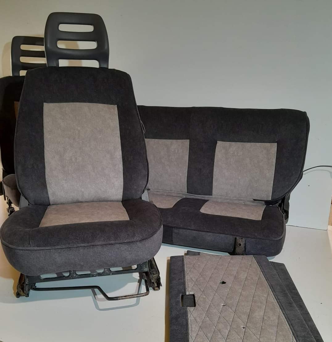 Zestaw wyjętych foteli samochodowych i tapicerki drzwi w odcieniach szarości, z widocznymi metalowymi elementami mocującymi.