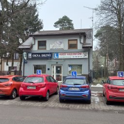 OSKK PEGAZ Zbigniew Muszyński - Budynek z szyldami 'Okna Drzwi', 'Kursy Motocyklowe', 'Kursy Kierowców', przed którym zaparkowane są cztery samochody z literą 'L' na dachu.