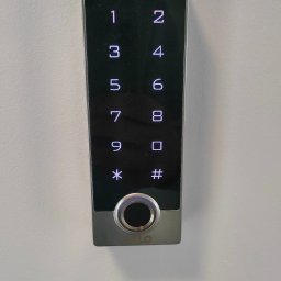 PS-Tech Piotr Skowronek - Panel dotykowy kontroli dostępu z czytnikiem linii papilarnych i klawiaturą numeryczną, zamontowany na białej ścianie.