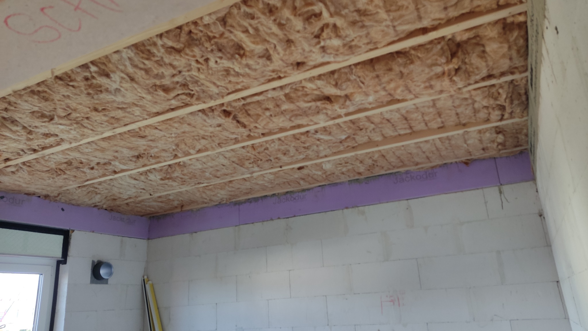 Poddasze w trakcie ocieplania, widoczne wełna mineralna między legarami, fioletowe płyty termoizolacyjne Jackodur przy ścianach z bloczków betonu komórkowego, surowy stan wykończenia.
