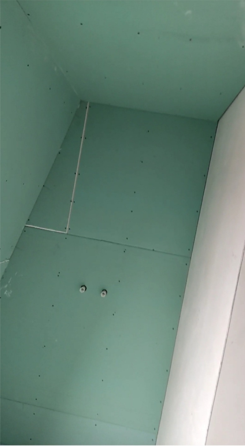 Ściana i sufit pokryte zielonymi płytami, widoczne czarne wkręty, biała ściana z boku, widoczne 2 uchwyty na suficie.