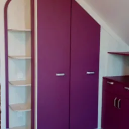 Fioletowa szafa wnękowa z półkami, dopasowana do skosu dachu, z jasną podłogą.