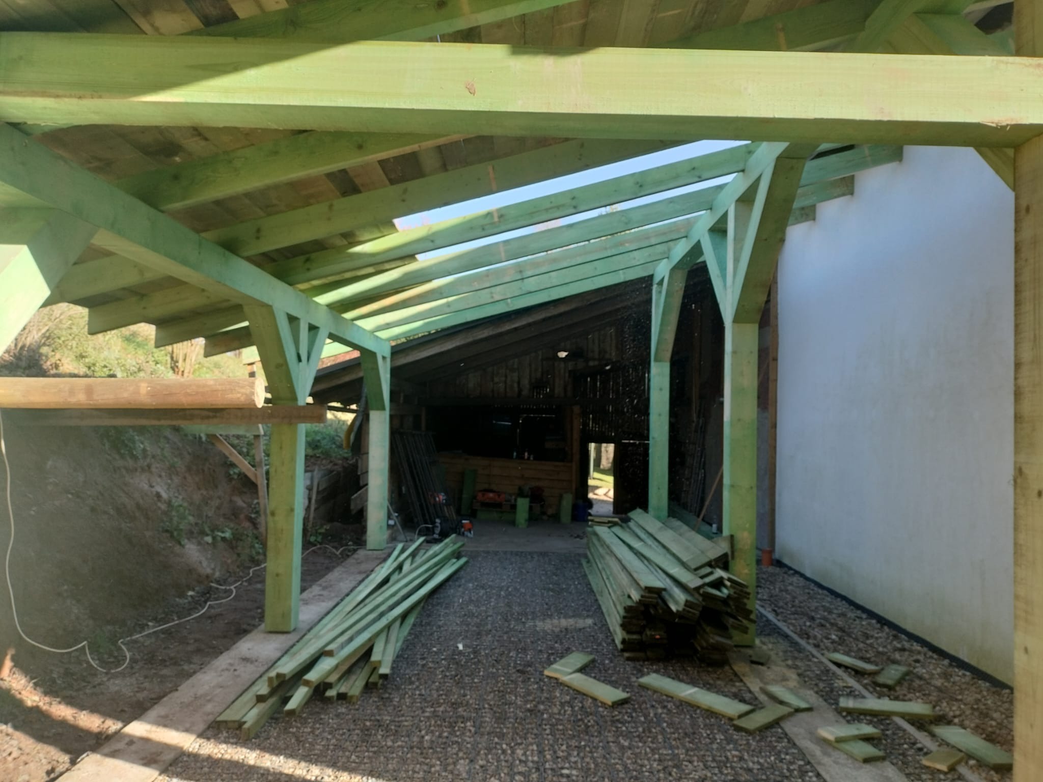 Konstrukcja z impregnowanego drewna, prawdopodobnie zadaszenie lub wiata, w trakcie budowy. Widoczne elementy drewniane i podłoże z kamieni.