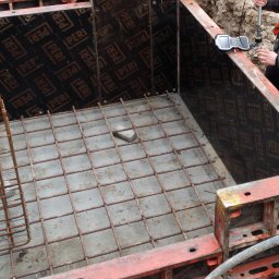 Usługi Geodezyjne GEOAR-2 - Przygotowany wykop z szalunkiem PERI, zbrojeniem dna i koszem zbrojeniowym, geodeta sprawdza poziom za pomocą niwelatora.